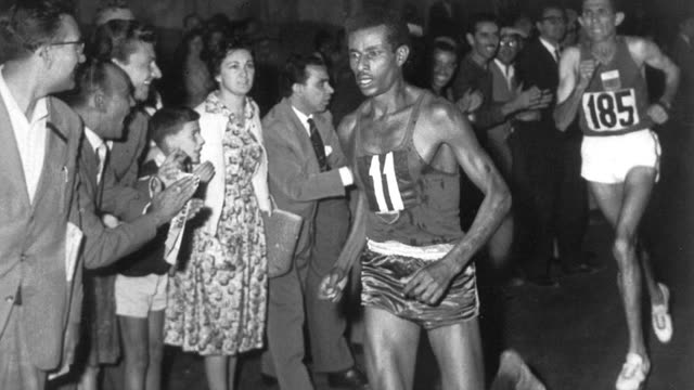 Abebe Bikila, wearing number 11, running barefoot through cheering crowds at night during the 1960 Rome Olympic marathon, with Rhadi Ben Abdesselam behind him