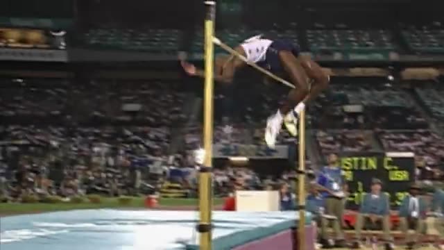 A high jumper arching backwards over the bar in a packed Olympic stadium